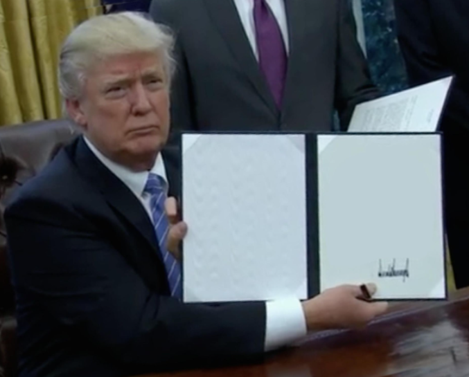 Donald Trump holding an executive order sign